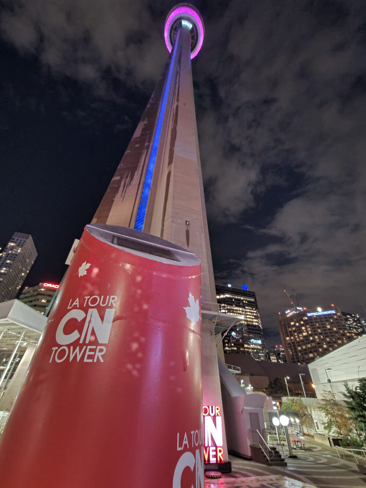 A looking-up shot of the CN Tower, showing the elevator windows glowing blue and the pod glass floor lighting shining purple