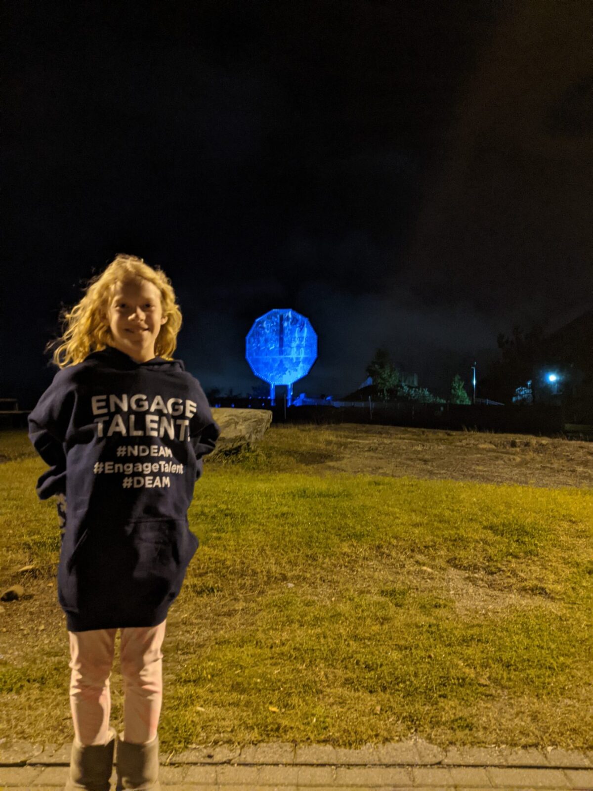 A girl standing in the foreground, smiling, with the Big Nickel shining blue in the background