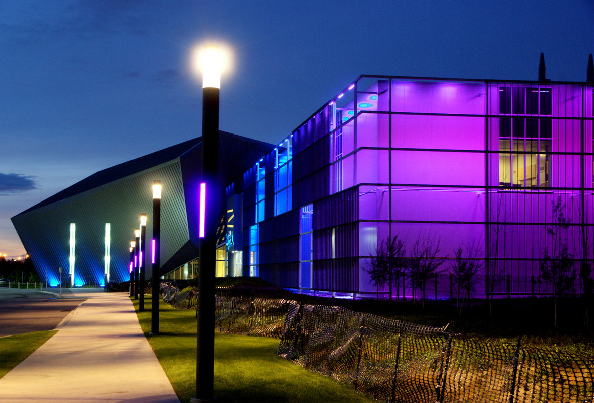 An evening shot of the Telus Spark Science Centre lit purple and blue, with a lamp-post glowing in the foreground.